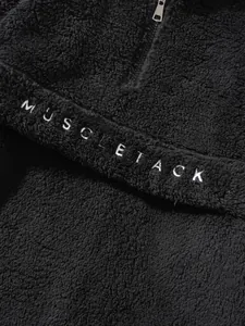 Detailed view of black fuzzy fleece pullover featuring MUSCLETACK letter embroidery