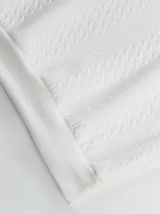 Detailed macro view of white jacquard knit fabric pattern and ribbed hem on men's top.