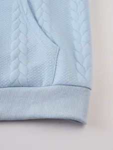Close-up of light blue jacquard hoodie featuring textured fabric and ribbed hem detail