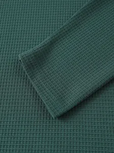 Detailansicht des dunkelgrünen Waffelstrickstoffs und der Ärmelbündchen eines Herren-Henleys.