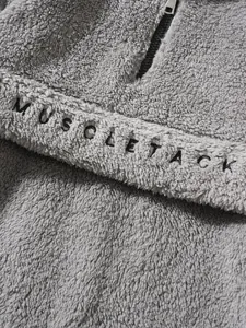 Macro detail of soft grey plush fleece sweatshirt with black MUSCLE TACK embroidery