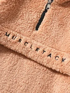 Detail view of brown plush fleece jacket featuring black 'MUSCLETACK' embroidery on chest