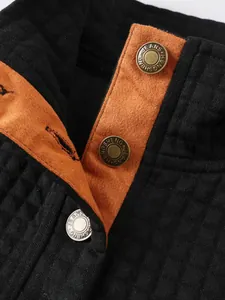 Primer plano del cuello alto y botones grabados en una sudadera negra con textura.