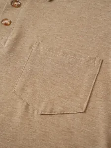Primer plano del bolsillo y los botones de un polo de punto marrón con tela texturizada.