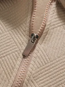 Nahaufnahme eines Metallreißverschlusses und strukturierten beigen Stoffs bei einem Poloshirt