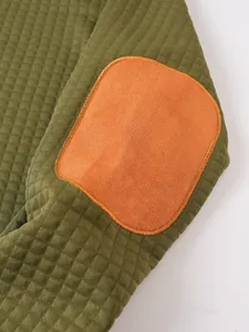 Primer plano de la manga de una sudadera verde oliva con textura de gofre y parche naranja