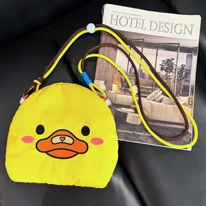Cute yellow duck cartoon mini crossbody bag with colorful rope strap next to a magazine.