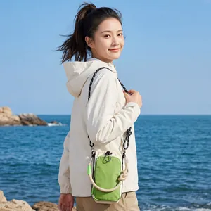 Asian model wearing a lightweight green and beige outdoor phone crossbody bag by the sea