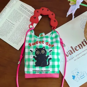 Close-up of a cartoon cat mini crossbody bag with green gingham and a red handle accent.