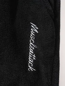 Close-up detail showing white Muscleattack embroidery on soft black fleece loungewear