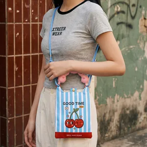 Detail view of a mini cartoon cherry crossbody bag styled with a casual grey T-shirt