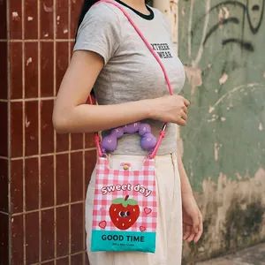 Detail view of pink checkered crossbody phone bag with strawberry graphic and purple handle.