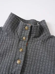 Detalle del cuello alto y botones de bronce en sudadera gris con diseño de rejilla cuadrada
