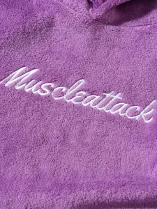 Close-up of white Muscleattack embroidery on soft purple plush pajama fabric texture