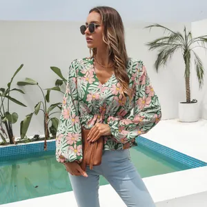 Model wearing floral V-neck chiffon blouse with lantern sleeves by an outdoor pool