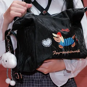 Detalle de bolso negro de nylon arrugado con bordado de teckel y colgante nube