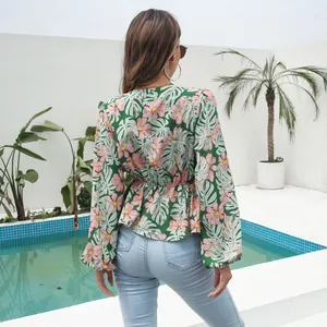 Back view of a green floral chiffon blouse with long lantern sleeves at a poolside.