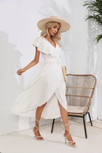 Full body view of a woman wearing a ruffled white maxi dress in a sunny resort setting