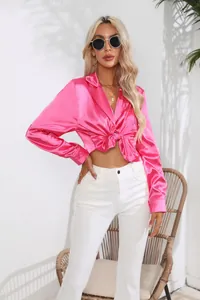 Detailansicht einer leuchtend rosa Satin-Langarmbluse, die für einen modischen Look geknotet ist