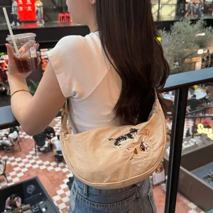 Beige crescent dumpling bag with cat embroidery and minimalist design