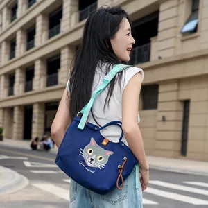 Stilvolle blaue Handtasche mit süßer Katzenstickerei, getragen von einer Frau im Freien