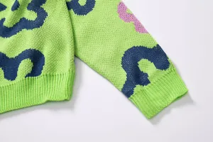 Close-up detail of lime green knitted sweater featuring floral jacquard and ribbed cuff texture.