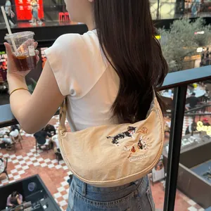 Detailed close-up of a beige embroidered dumpling bag worn by a model in a lifestyle setting