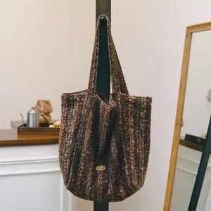 Large brown bouclé wool tote bag with green stripes hanging on a display stand.
