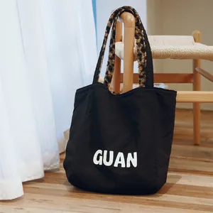 Close-up of a black reversible tote bag with stylish leopard print handles and GUAN logo