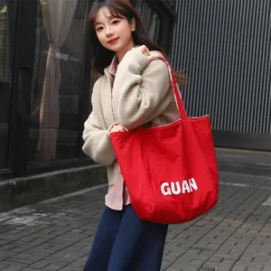 Minimalist large red fabric tote bag with GUAN print shown on a model in urban setting