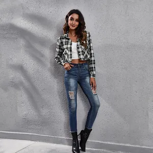 Volledig beeld van een vrouw in een geruit kort jasje met modieuze gescheurde jeans.
