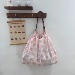Sac fourre-tout blanc brodé de fleurs roses suspendu à un crochet mural en bois minimaliste.