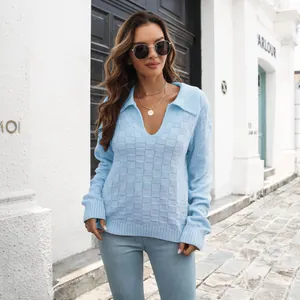 Dettaglio di un maglione polo da donna azzurro con trama a scacchi 3D in un ambiente urbano.