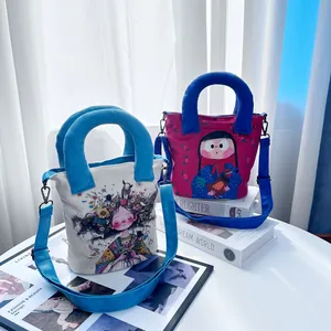 Cute hand-drawn girl canvas bucket bags with blue handles and straps on a white table