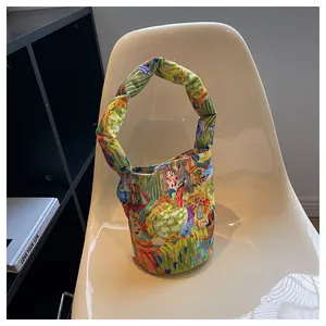 Bolso de lona artístico tipo cubo con estampados coloridos en una silla de diseño blanca.