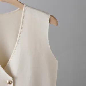 Detailed macro view of the cream knit fabric and golden button of the slim vest