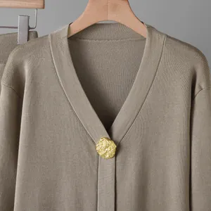 Détail d'un cardigan en maille kaki avec un bouton métallique doré texturé et martelé