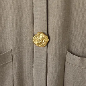 Gros plan d'un bouton en métal doré irrégulier sur un cardigan en maille de couleur taupe