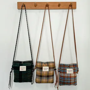 Detailed view of three plaid wool crossbody bags in various colors on a wooden hanger