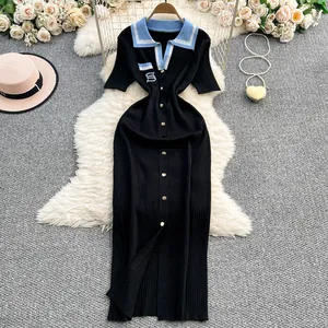Detalle de un vestido de punto polo negro con cuello azul y bordado de la letra S.