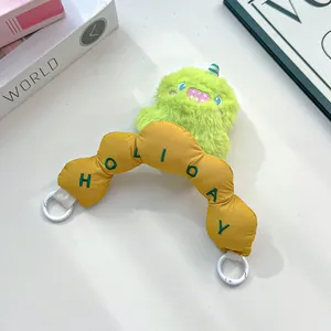 Detail view of a green plush monster charm with a yellow embroidered 'HOLIDAY' handle.