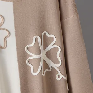 Close-up detail of beige colorblock knit sweater with white floral embroidery texture.