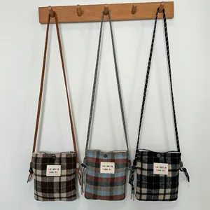 Selection of three woolen plaid crossbody bags in various colors hanging on a wooden rack