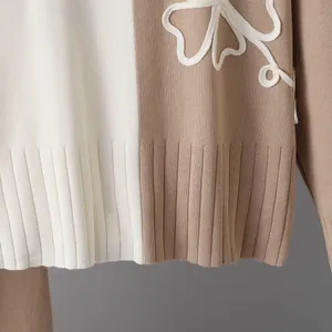 Close-up of color-block knit top showing ribbed hem and white floral embroidery.