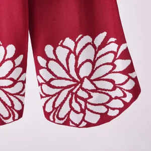 Primo piano del complesso motivo jacquard floreale bianco sul polsino della manica in maglia rossa