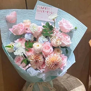 Elegant floral bouquet wrapped in light blue pleated crinkle paper with pink roses