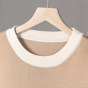 Primer plano de un suéter de punto de cuello redondo bicolor en beige y blanco en percha