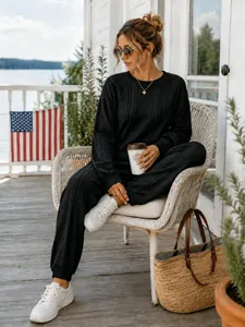Lifestyle detail of woman in black cable-knit sweater and jogger pants set on sunny porch