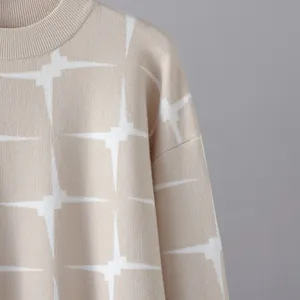 Close-up of beige knitted sweater detail with white star jacquard pattern and rib neck.