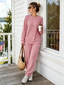 Stylish pink cable-knit two-piece lounge set with crewneck top and pants on a porch.